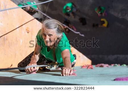 Aged Lady Doing Extreme Sport Elderly Female Makes Hard Move on Outdoor Climbing Wall Sporty Clothing on Fitness Training Intense but Positive Face Using Rope and Belaying Gear