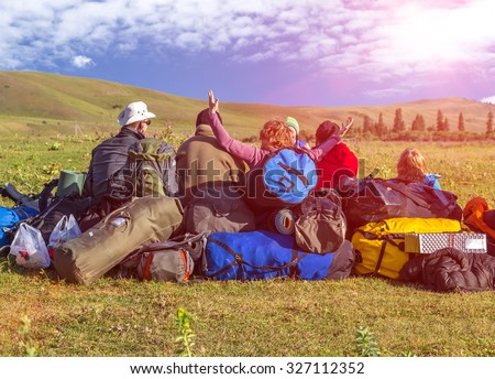 Jolly Company of Tourists Sitting on Large Heap of Travel Luggage on Green Meadow of Wild Kirghiz Steppe Expressing Joy and Amazement Shining Sun above Hills on Blue Sky