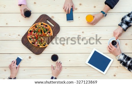 Company of Friends at Cafe Pizza Table Top View of Natural Wooden Desk with Pizza and Hands of Group of People with Drinks and Electronic Gadgets Casual Clothing