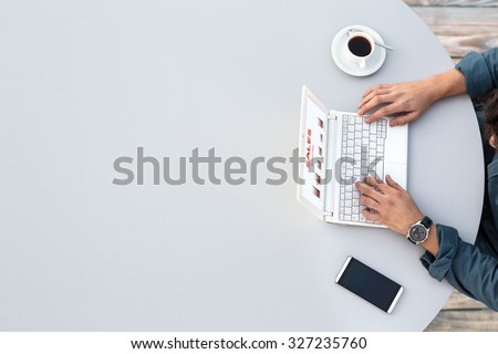 White Office Round Table and Man Working on Computer Top View Casual Clothing Typing on Keyboard with Marketing Chart on Screen Smart Phone and Cup of Coffee aside