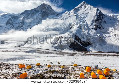 Base Camp of High Altitude Mountain Expedition Many Orange Tents Located on Side Rock Moraine of Glacier in Severe Snow and Ice Peaks Landscape