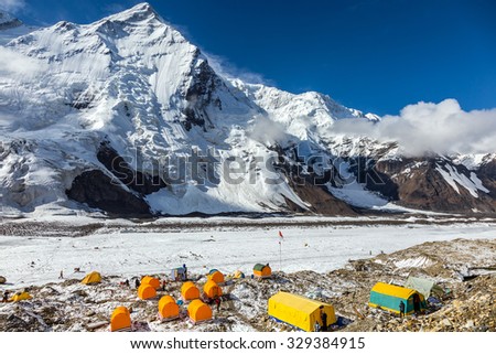 Base Camp of High Altitude Mountain Expedition Many Orange Tents Located on Side Rock Moraine of Glacier in Severe Snow and Ice Peaks Landscape