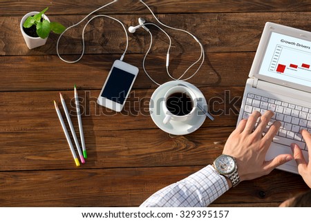 Business at unusual desk concept Man working on computer presentation sitting at unusual handcrafted rough wooden desk overhead top view coffee mug with many office supplies in creative disorder