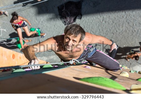 Smiling Mature Man on Extreme Climbing Wall\
Portrait of Handsome Adult Male Climber Moving Up on Sport Training Course in Outdoor Climb Gym\
Using Rope Belaying Gear with Positive Inspired Face Emotion