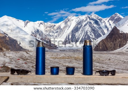 Active Lifestyle Couple Concept Two Blue Travel Thermoses Cups and Sunglasses on Wood Table and Mountain Landscape Focus on Mountains Thermoses are Blurred