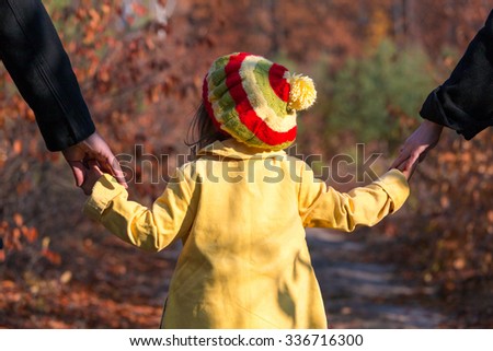 Young Family Walking on Park Alley Parents Holding Hands of Little Baby Daughter from both Sides Autumnal Colorful Forest on Background