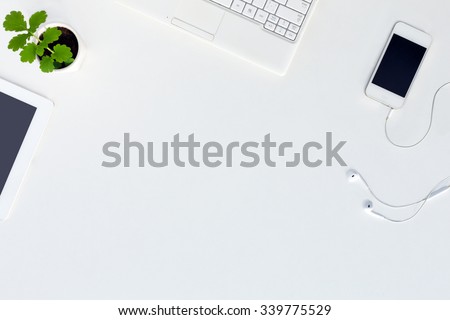 Top View of trendy White Office Desk with white Cropped Laptop Tablet Telephone Earphones Electronics and green Flower