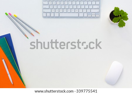 Creative Office White Table with Color Orange Green Blue Magazines and Pencils Computer Keyboard Mouse and Green Flower Top View