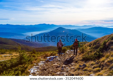 Man and Woman Hikers sportive Couple walking on rural Road or Trail from rear point scenic View of smoky stacked Mountain Ridges and evening light of Sunset