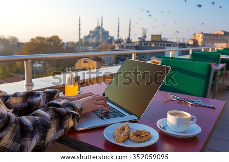 Working Breakfast Person Working on Laptop Computer at Cafe Terrace on Table with Coffee Mug Orange Juice and Bakery Cookies Asian Urban Landscape Sultan Ahmed Mosque and Birds flying on background