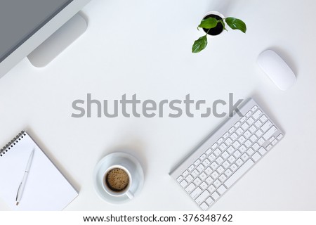 Top View of Modern Technology working Place on White Office Desk with large Desktop Computer Coffee Mug Keyboard and Mouse green Flower Notepad and Pen
