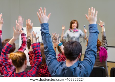 Diverse Group of Students in Conference Room raising Arms up actively participating in Seminar Teachers Body on background