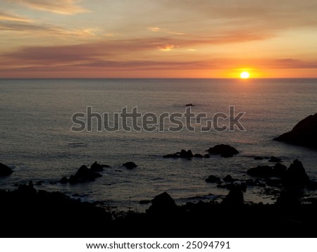The sun appears as a blazing ball of fire as it sets on the ocean horizon