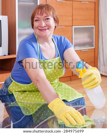 Mature woman  dusting furniture   with detergent polish at home
