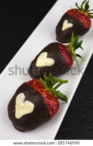 red strawberry dipped in dark chocolate decorated with heart of white chocolate