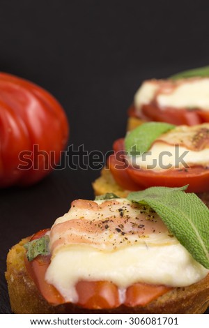 bruschetta with tomato and mozzarella wrapped in a slice of bacon with sage and pepper