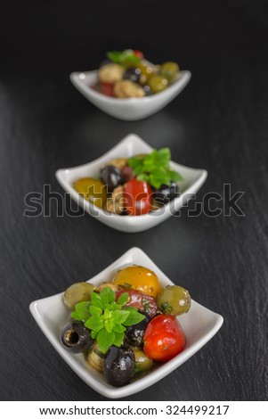 Mediterranean antipasti salad with mozzarella balls, green and black olives and cherry tomatoes and some tiny-leafed basil.