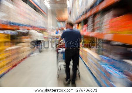 Male shopper pushing a shopping cart in a large grocery store. Image is blurred to imply motion, activity, and stress.