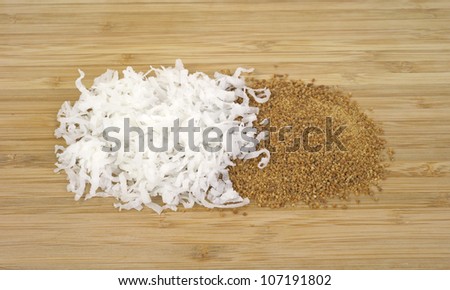 A portion of white shredded coconut and brown coconut sugar on a wood cutting board.