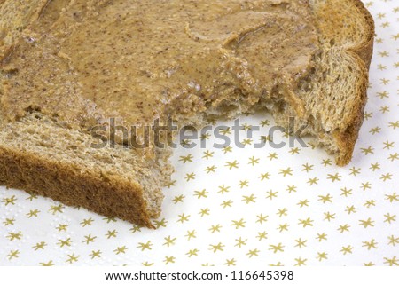 Close view of a piece of wheat toast with almond butter that has been bitten on a paper napkin.