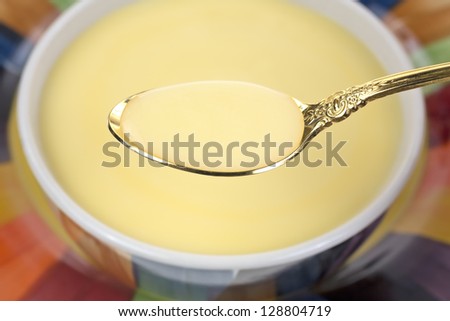 A bowl of cheddar cheese soup in the background with a gold spoonful of soup in the foreground.