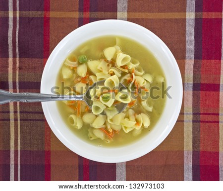 A bowl of vegetables and pasta chicken broth soup with spoonful on a colorful cloth background.