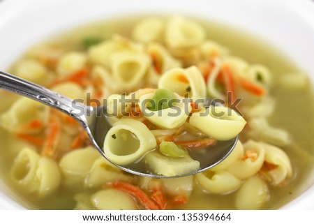 Close view of a spoonful of pasta vegetable chicken broth soup with the remainder of the meal in a bowl in the background.