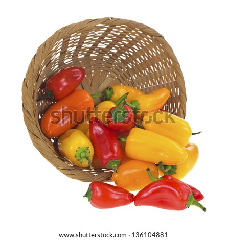 A wicker basket on it\'s side spilling several small sweet peppers onto a white background.