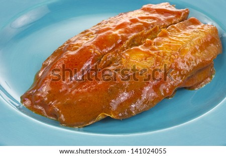 A fillet of smoked herring covered with tomato sauce on a blue plate.