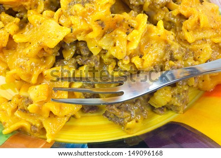 A very close view of a home cooked meal of pasta in a cheese sauce with cooked ground beef on a colorful plate with fork.