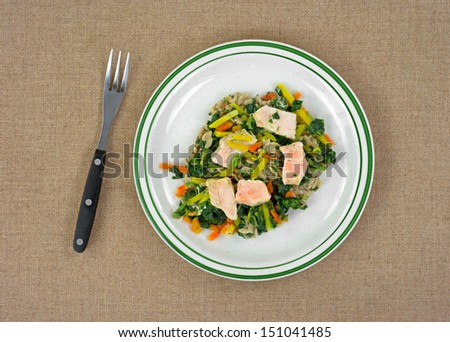 Top view of a cooked TV dinner of salmon with carrots and spinach on pasta with fork.