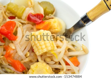 Close view of a small bowl with oriental type vegetables and noodles with a fork on a white background.
