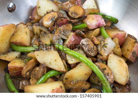 A very close view of red potatoes, green beans, onions and mushrooms cooking in a stainless steel skillet.