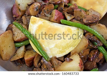 A very close view of vegetables and pierogies cooking in a stainless steel skillet.
