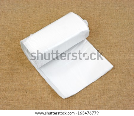 A slightly opened roll of plastic wrap or sheeting on a tan cloth background.