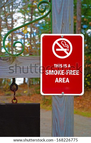 A red and white smoke-free area sign on a wood post.