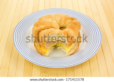 Bitten sausage egg and cheese croissant breakfast sandwich on a blue striped plate atop a bamboo place mat.