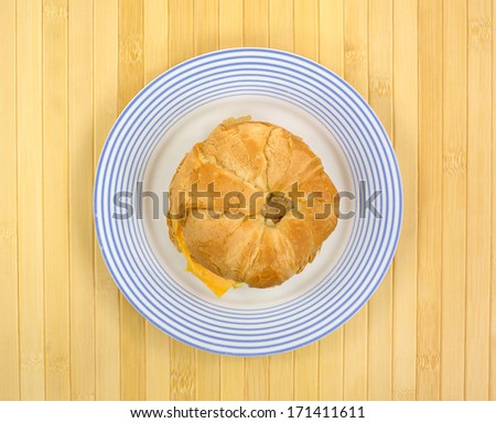 Top view of a croissant breakfast sandwich on an old chipped blue striped plate atop a bamboo place mat.