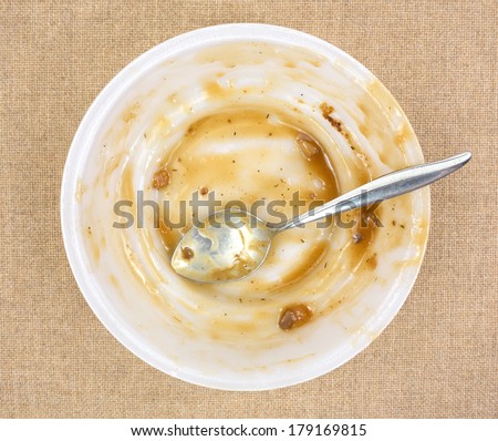 Top view of a finished TV dinner bowl with a spoon on a cloth background.
