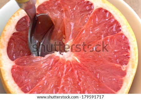 Close view of a halved red grapefruit in a bowl with a spoon inserted in the pulp.