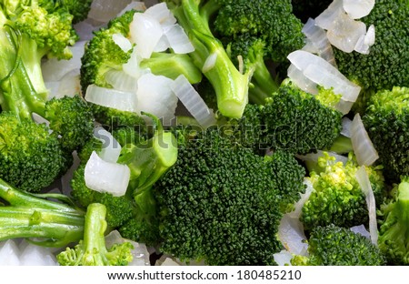 A very close view of fresh broccoli florets and sliced sweet onions cooking in a skillet.