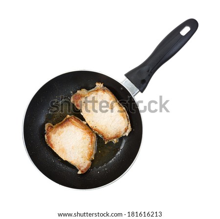 Top view of two small pork loin steaks frying in a skillet on a white background.