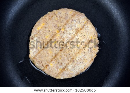 Close view of a single vegetable burger patty cooking in skillet.