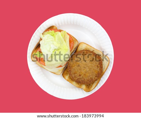 Top view of an open faced veggie burger patty on a paper plate with onions tomatoes and lettuce atop a red background.
