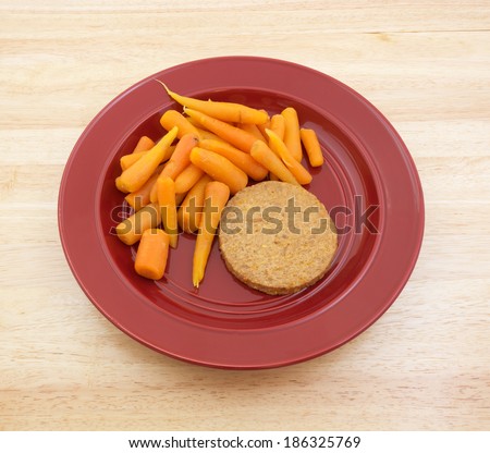 A diet meal consisting of a vegetable burger patty with carrots on a red plate atop a wood tabletop.