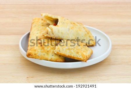 A small plate of two pasties stuffed sandwiches with one bitten on a wood counter top.