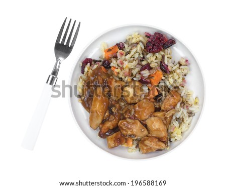 Top view of a cooked TV dinner with chicken in a pecan sauce, rice and cranberries in a small plate with fork to the side.