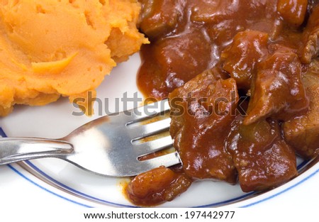 A blue striped plate with braised beef in a sauce and sweet potatoes with fork.