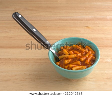 A serving of macaroni in tomato sauce with beef chunks in a green bowl with spoon on a wood table top.