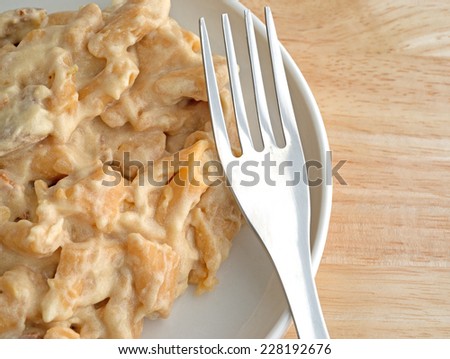 Top view of plate of chicken in pasta with a thick jalapeno pepper sauce with a fork on a wood table top.